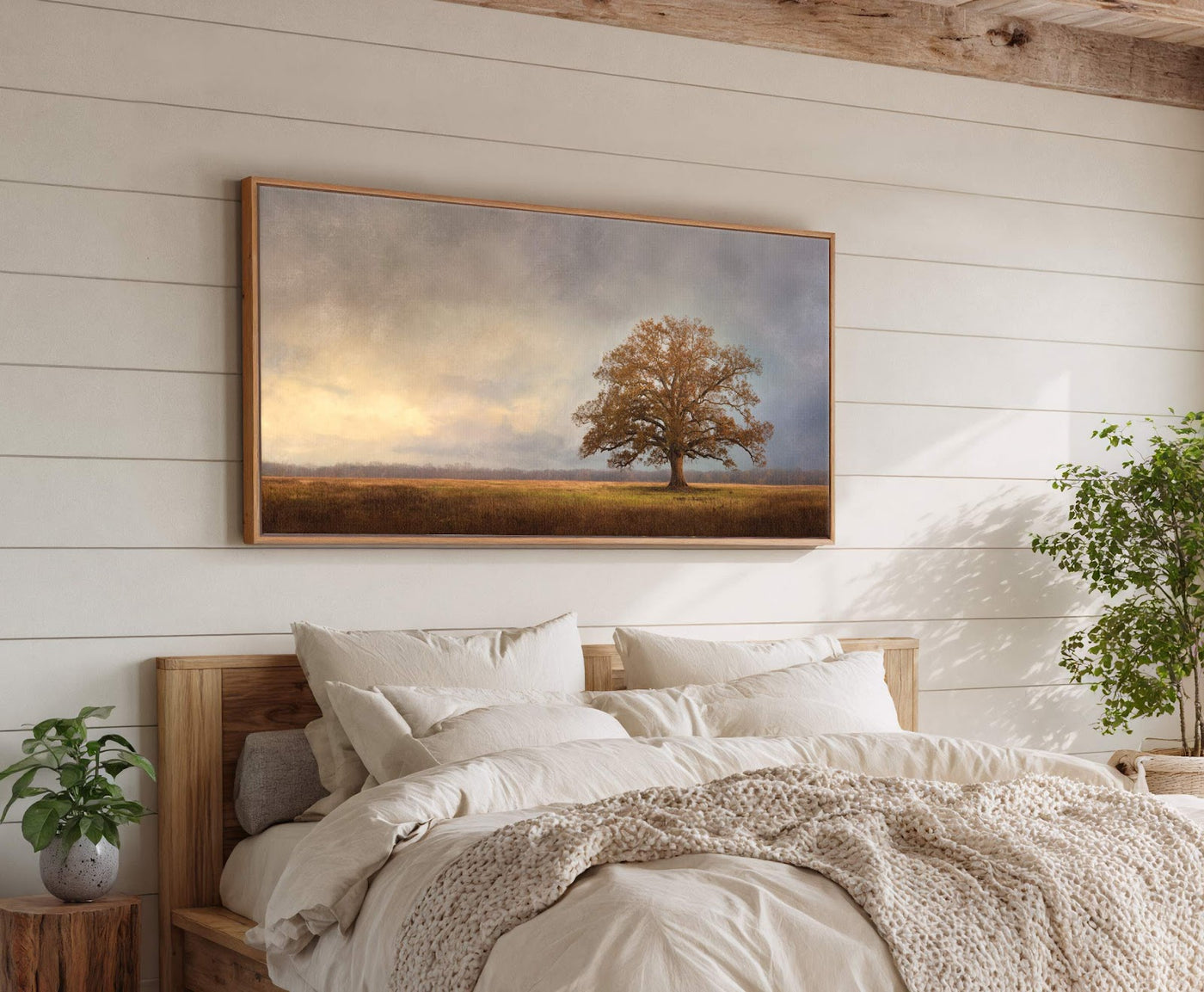 This horizontal canvas wall art features a lone tree in a field under a cloudy sky with warm light. The artwork is displayed above a bed with pillows on a.