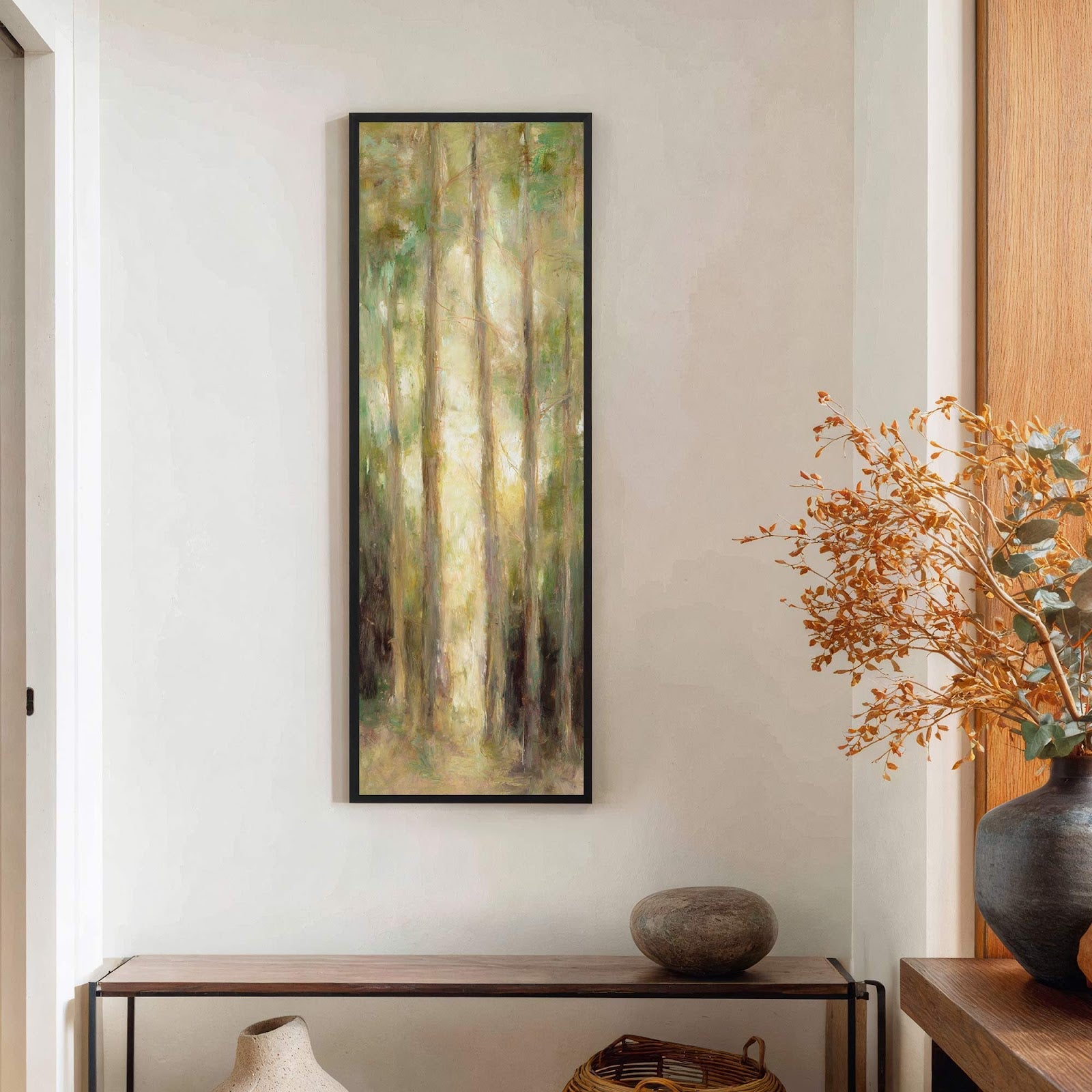 This vertical painting print features a sunlit forest scene with a palette of greens and yellows, displayed in a black floater frame above a wooden console table on a neutral.