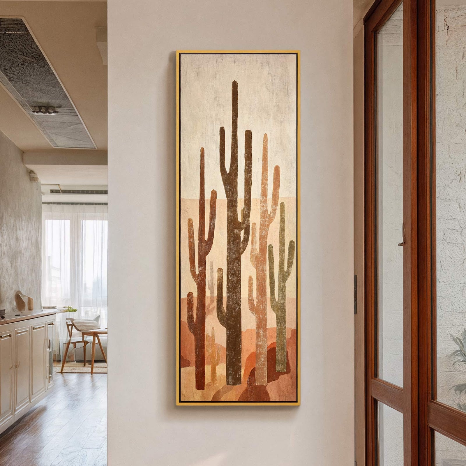 This vertical canvas wall art features an abstract desert landscape with saguaro cacti in warm earth tones and a golden floater frame, displayed on a light-colored wall near a wooden.