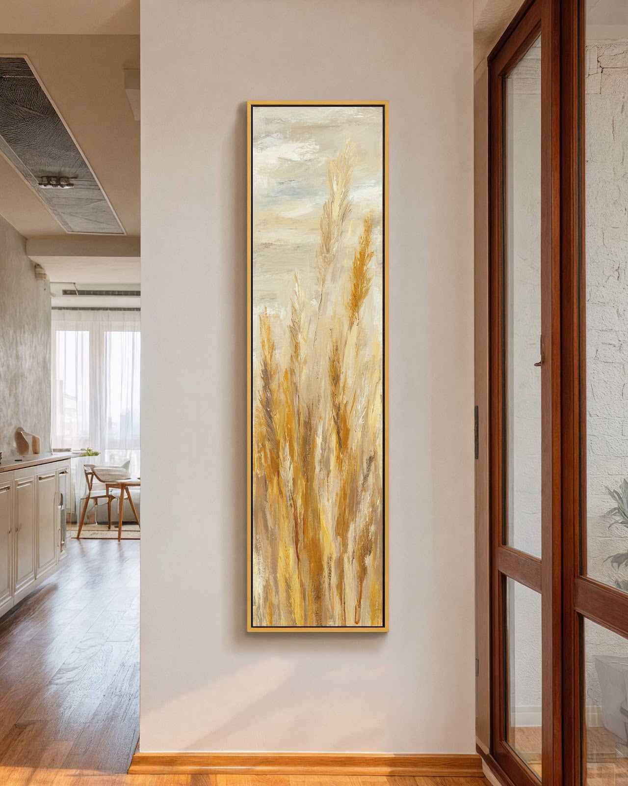 This vertical impressionist pampas grass painting print in a warm golden palette is mounted on a white wall in a hallway near a window, featuring a gold floater frame.