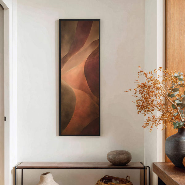 This vertical canvas wall art features abstract shapes in a warm palette of browns and oranges, framed in black, hanging above a wooden console table with a vase and a.