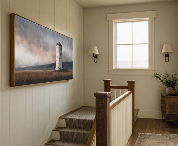 This horizontal canvas wall art features a lighthouse with a subdued, painterly style and a palette of grays, browns, and muted pinks. It hangs on a neutral, paneled wall in.