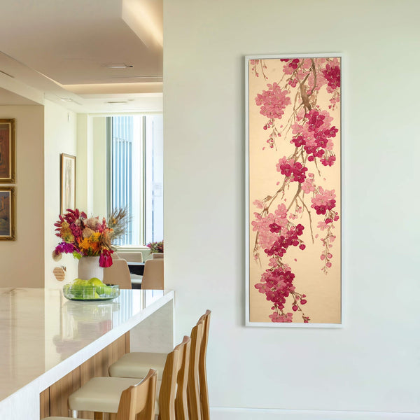 A vertical canvas wall art print of pink cherry blossoms with a gold background is displayed on a white wall, with chairs visible in the background.