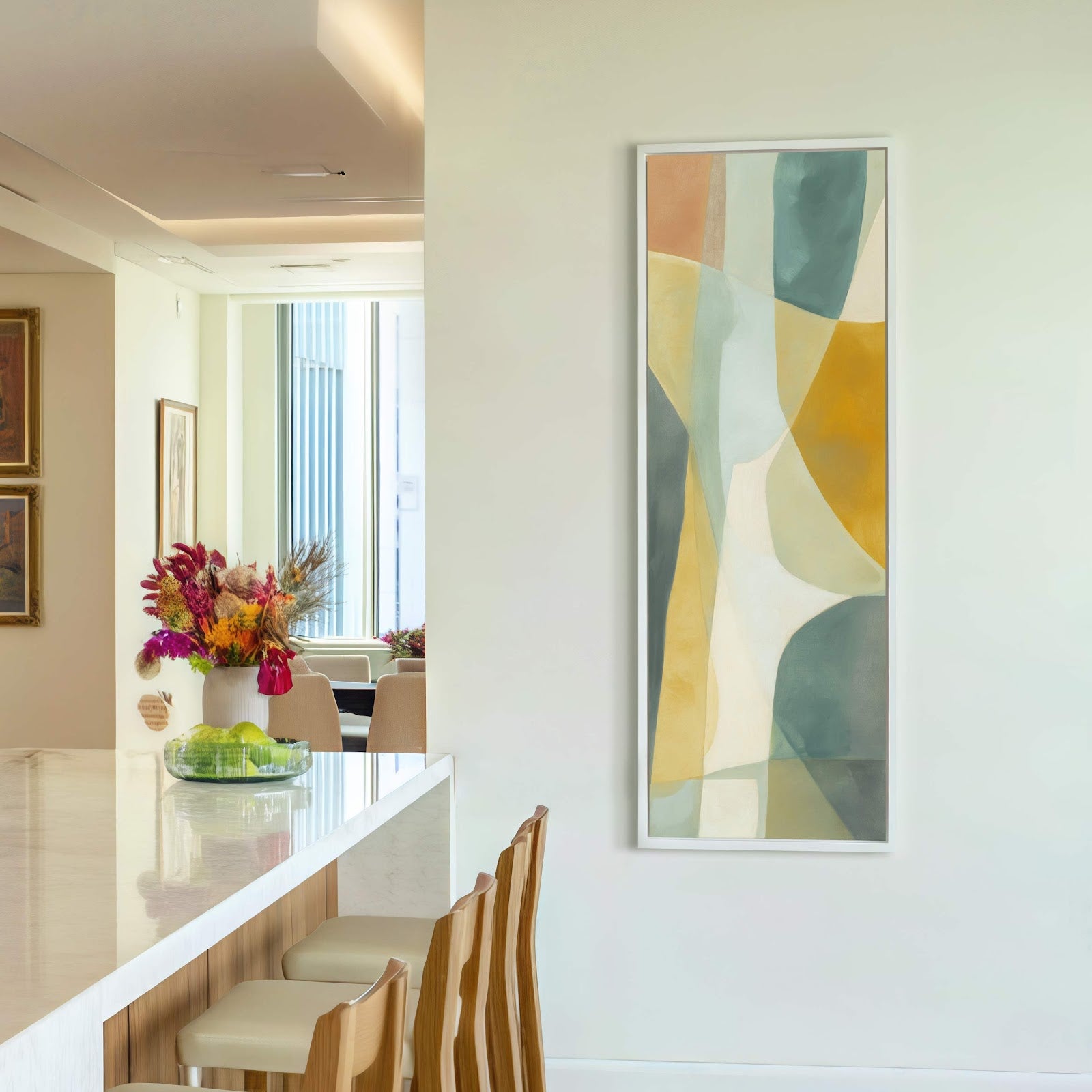 This vertical canvas print features abstract shapes in a palette of muted earthy tones and teal, framed in white, displayed on a white wall above a counter with bar with.