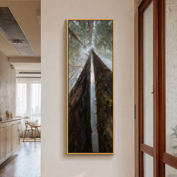 This vertical canvas wall art features a dramatic low-angle view of towering trees with a palette of dark browns and lush greens, framed in gold and displayed in a room.
