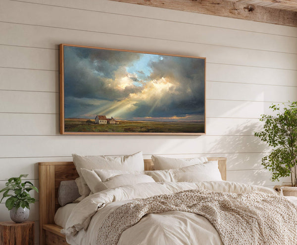 This horizontal canvas wall art features a dramatic landscape painting with stormy clouds and sunbeams illuminating two houses in a field, framed in natural wood and displayed above a bed.