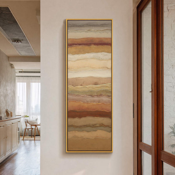 This vertical canvas wall art features an abstract, layered design with a warm earth-toned palette. It hangs on a neutral wall in a hallway, next to a wooden door frame.