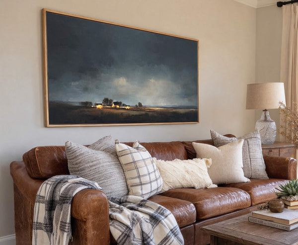 This horizontal canvas wall art features a moody landscape with distant farmhouses lit by warm lights under a dramatic sky, rendered in dark blues and earthy tones in a painterly.