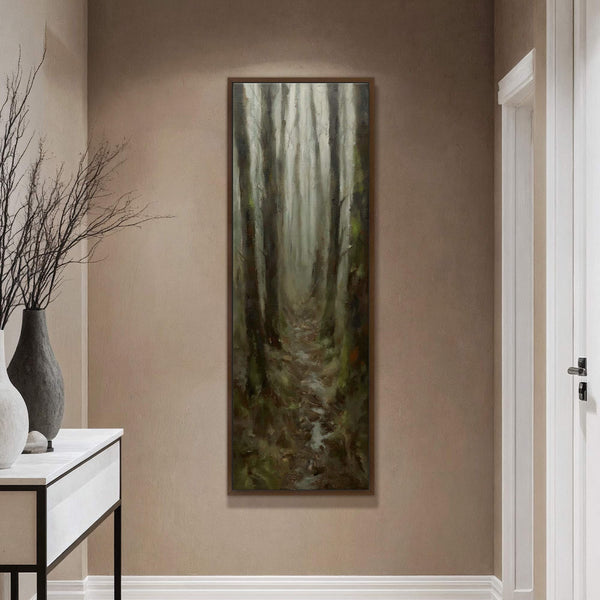 This vertical canvas wall art, featuring a dark, moody forest path in an impressionistic style, hangs in a room with tan walls next to a console table with vases.