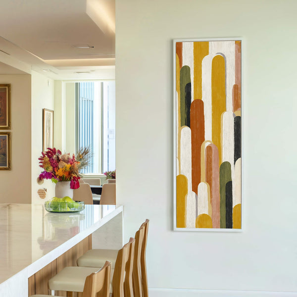 This vertical canvas wall art features an abstract design with a palette of mustard yellow, rust orange, and muted green. It is framed in white and hangs on a white.