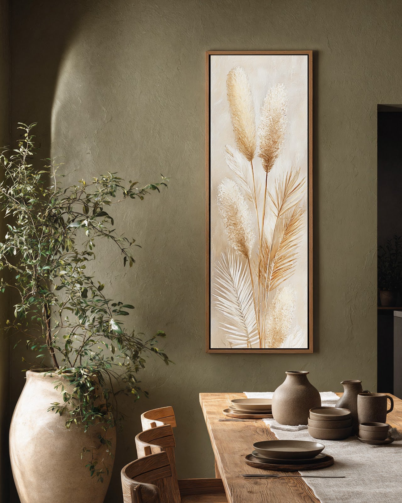 This vertical canvas wall art depicts textured pampas grass in a cream palette, housed in an oak floater frame on an olive green wall beside a rustic dining table.