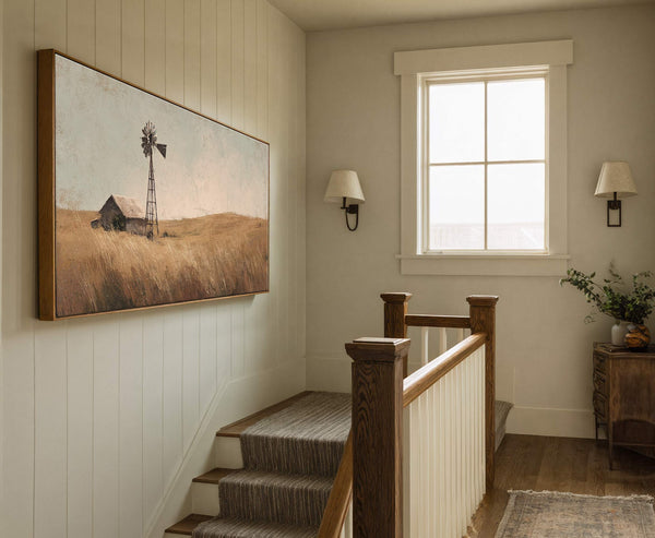 This horizontal, landscape-oriented canvas wall art features a rustic windmill and barn in a sepia-toned, impressionistic style, set against a hazy sky and dry grass, displayed on a paneled wall.