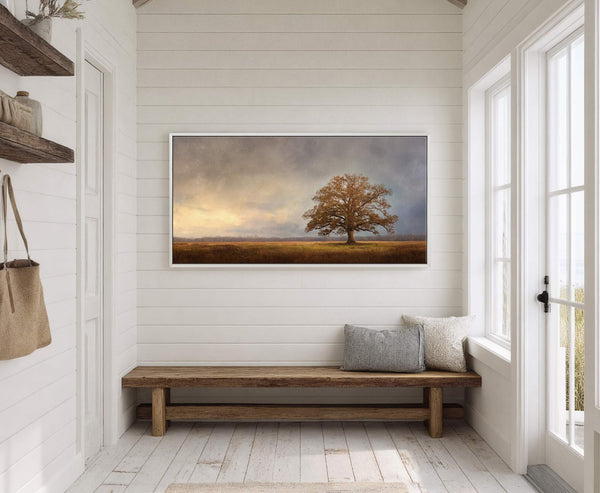 This horizontal canvas wall art features a rustic, solitary tree in a field with a dramatic, textured sky and a warm, earthy palette, displayed in a room with white paneled.