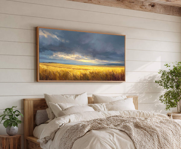 This horizontal canvas wall art depicts a golden wheat field under a dramatic sky, rendered in an impressionistic style. It is displayed above a bed on a white paneled wall.