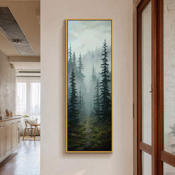 This vertical canvas wall art displays a misty forest path in dark greens and blues. The painting print is framed in gold and hangs on a cream-colored wall next to.