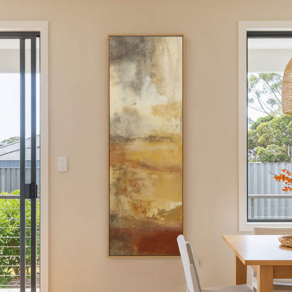 This vertical abstract art print features a rich palette of earthy browns, yellows, and grays with a textured, layered style, displayed in a natural wood floater frame in a dining.
