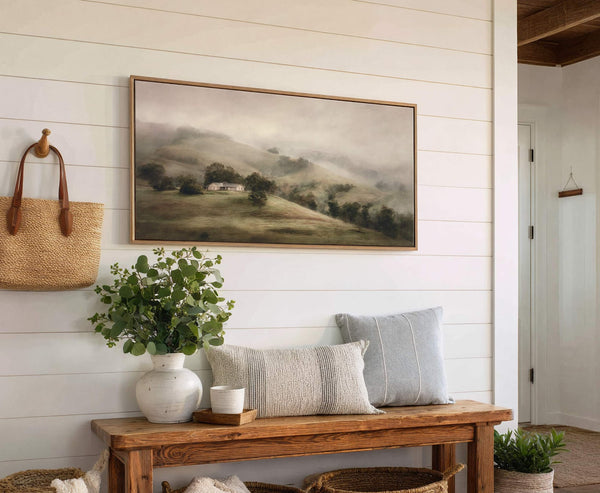 This horizontal canvas wall art features a misty landscape with rolling green hills and a farmhouse, rendered in a muted green and gray palette with a loose, painterly style. The.