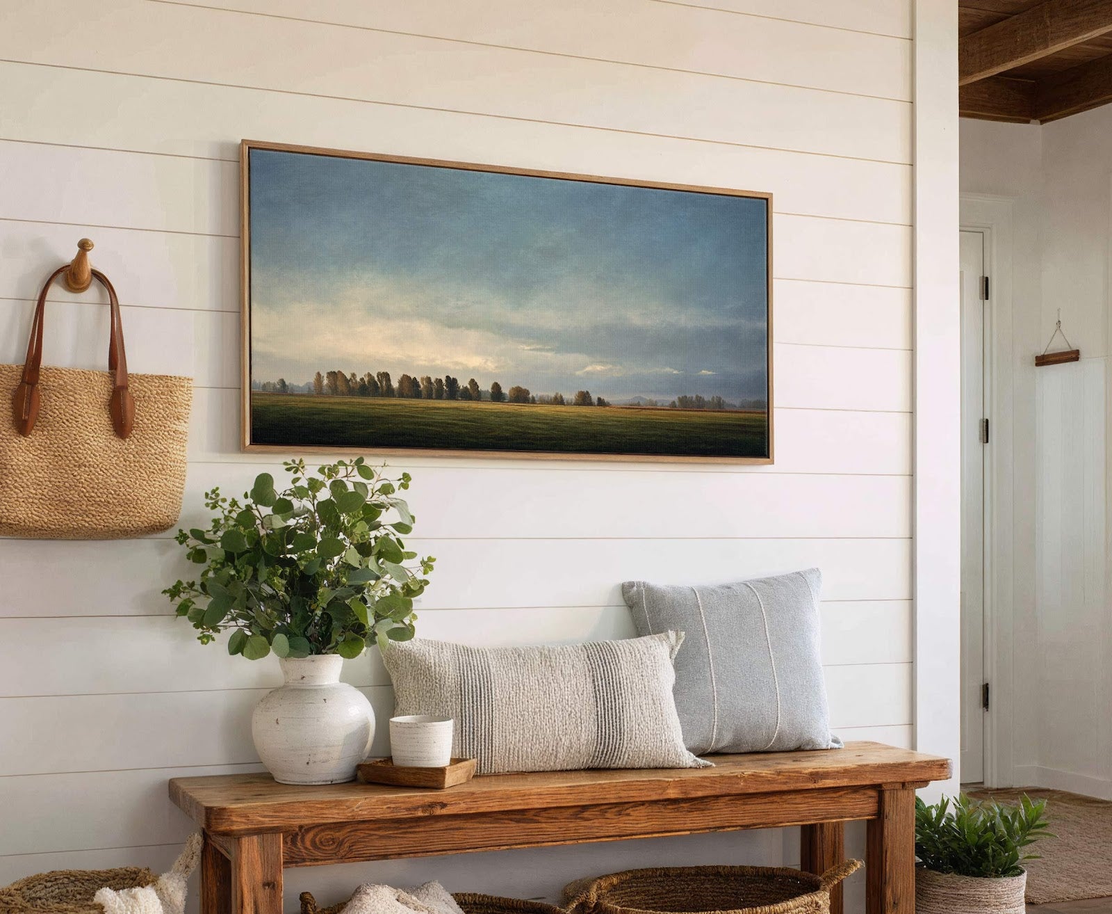 This horizontal canvas wall art print depicts a hazy landscape with trees against a cloudy sky, rendered in muted greens and blues. It is displayed on a white shiplap wall.