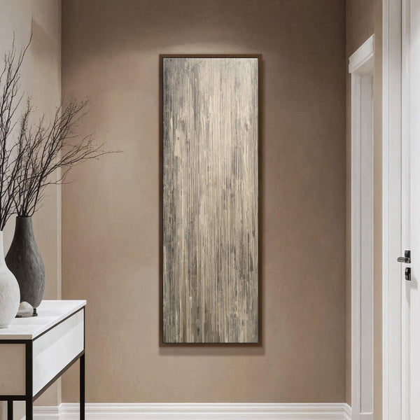 This vertical canvas wall art displays an abstract texture with vertical lines in a neutral palette and is framed in dark wood, hanging on a taupe wall above a console.
