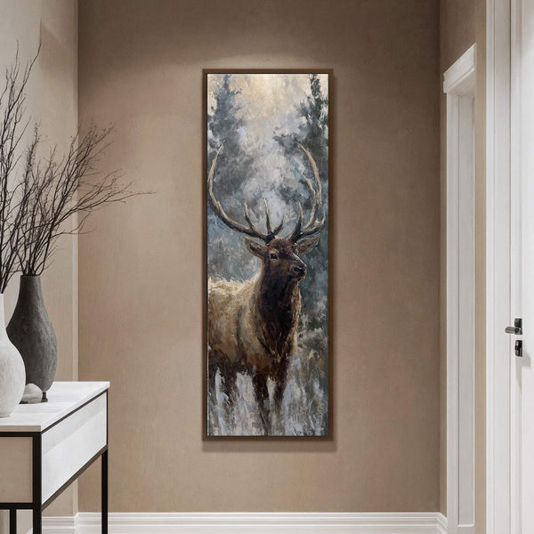This vertical canvas wall art depicts a majestic elk in a forest with a muted color palette and loose brushstrokes, framed in dark wood and hanging on a taupe wall.