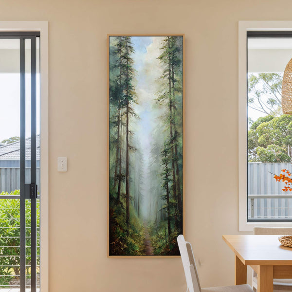 This vertical, framed canvas print displays a realistic forest scene with tall pine trees and a path, rendered in a palette of greens and blues. It hangs on a cream.