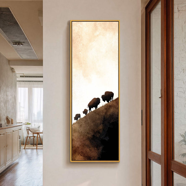 This vertical canvas wall art features a minimalist silhouette style with a warm, earthy palette of browns and beiges, depicting a herd of bison ascending a hill under a gradient.
