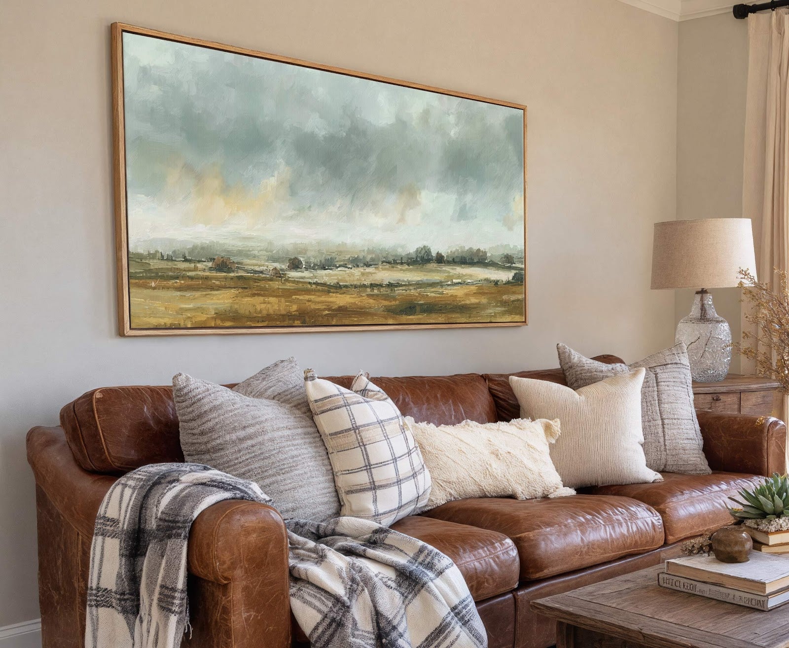 This horizontal canvas wall art features a landscape with a muted palette of blues, greens, and golds in a painterly style. It is displayed above a brown leather sofa on.