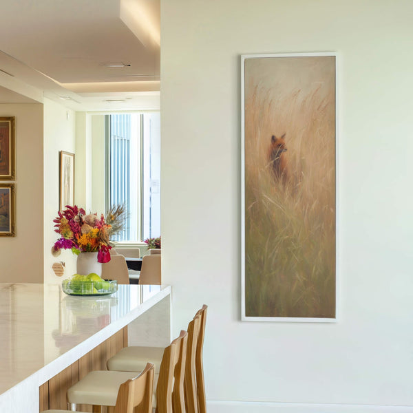 This vertical canvas print features a fox peeking through tall grasses in a warm, earthy palette. The art is displayed on a plain white wall, adjacent to a dining area.