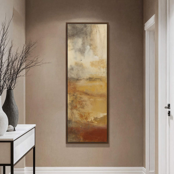 This vertical, abstract art print features a warm, earthy palette with textures resembling a landscape. It is displayed on a taupe wall above a console table with decorative vases.