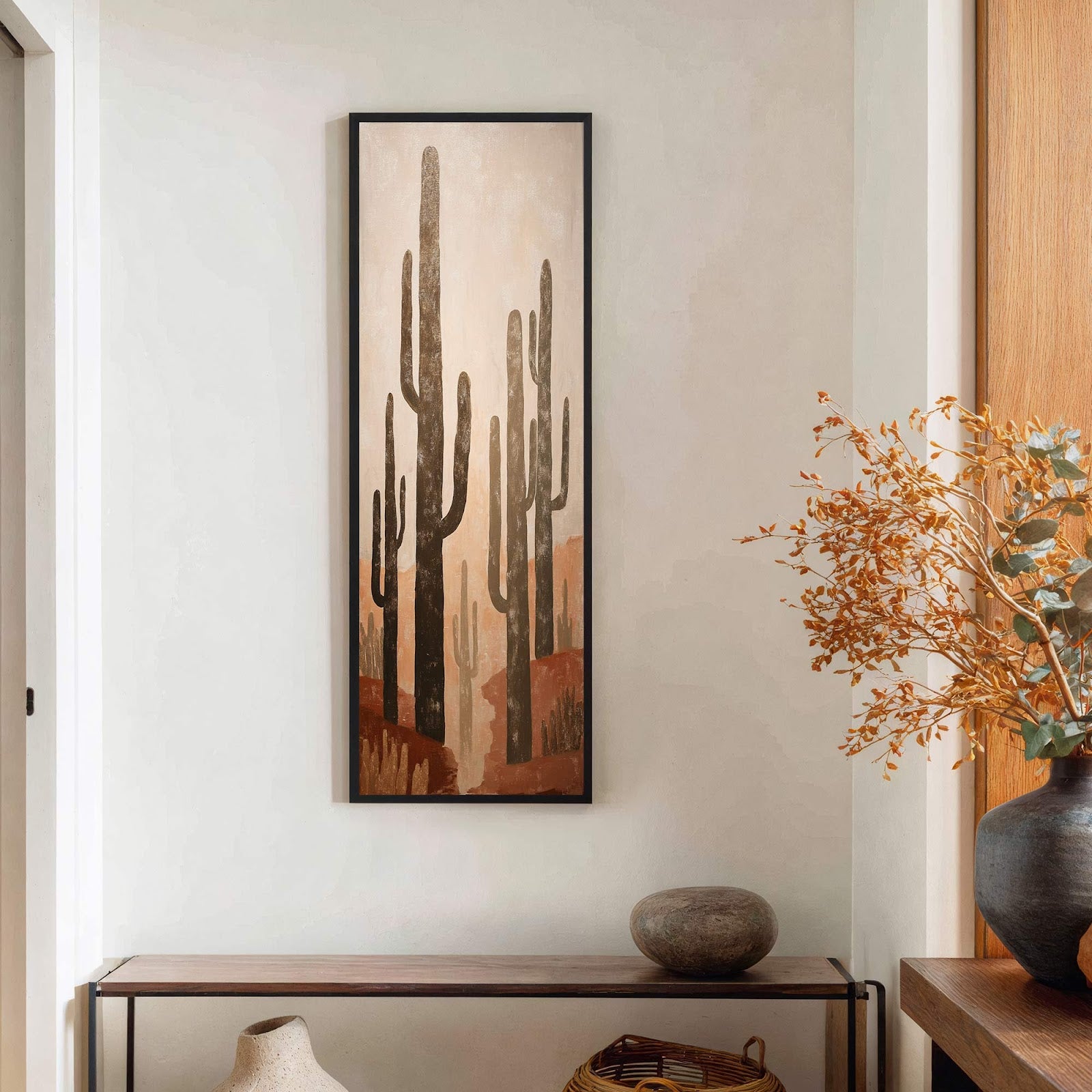 This vertical canvas wall art features a desert landscape with saguaro cacti in a muted palette of browns and tans, framed in black, hanging above a narrow wooden console table.