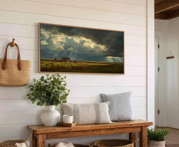 This horizontal canvas wall art depicts a dramatic landscape with stormy skies over a rural field and barn, featuring a dark and light palette. The art print is framed in.