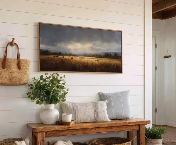 This landscape art print features a muted palette of grays and golden browns, capturing hay bales in a field under a dramatic sky. It is a horizontal, stretched canvas print.