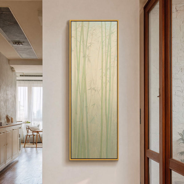 This vertical canvas wall art features a serene bamboo forest rendered in a muted green and beige palette with a minimalist style, framed in gold and hanging on a cream-colored.