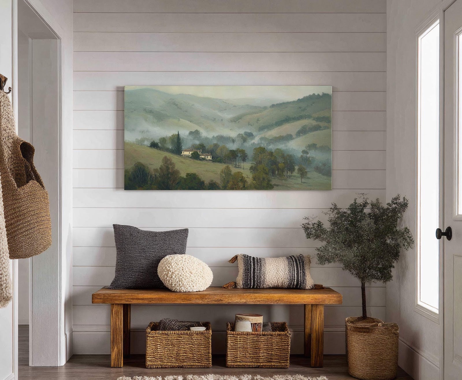 This horizontal canvas wall art depicts a misty, pastoral landscape with muted green and beige tones in a painterly style, displayed above a wooden bench with cushions and baskets in.
