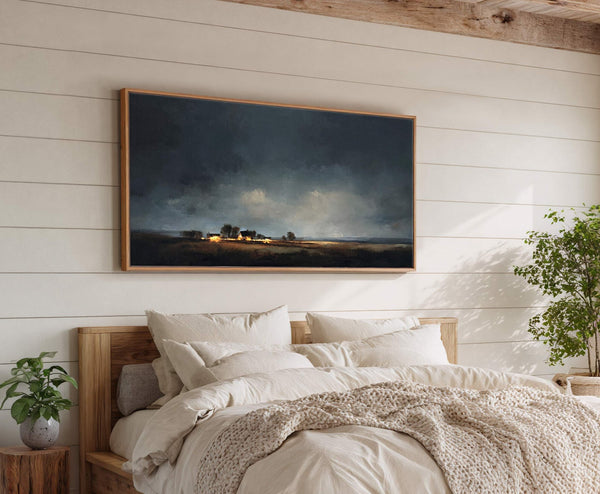 This horizontal canvas wall art depicts a moody landscape of distant, glowing farmhouses under a dark, cloudy sky, with a natural wood floater frame, set against a white shiplap wall.