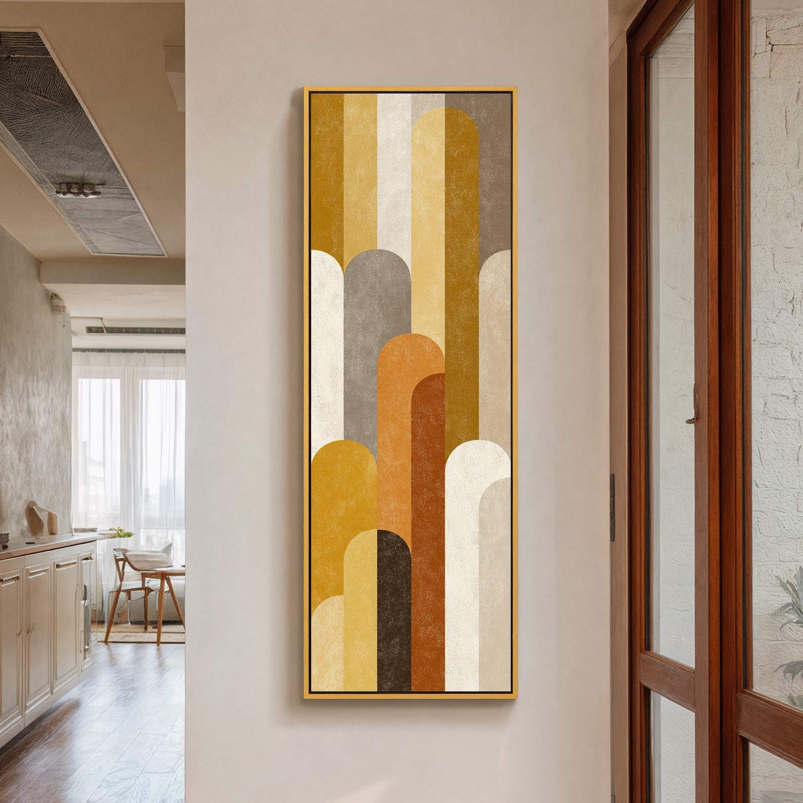 This vertical canvas wall art features an abstract geometric design with a warm palette of mustard yellow, brown, and cream, framed in gold and hanging on a beige wall near.
