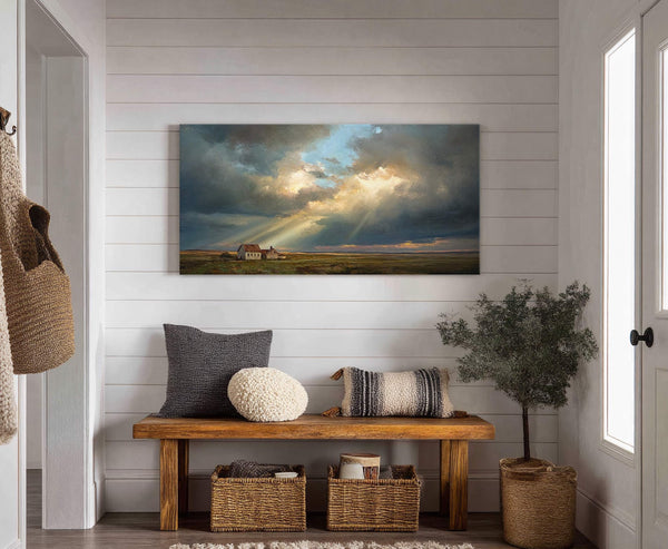This horizontal canvas print displays a dramatic landscape with a farmhouse under a stormy sky with sunbeams breaking through, set against a backdrop of white shiplap walls and a wooden.