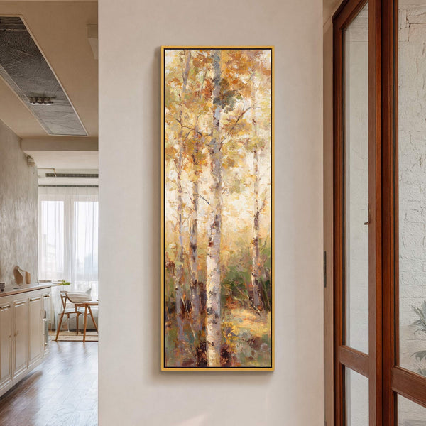 This vertical, impressionistic art print depicts a sun-drenched birch forest in warm yellows and greens, framed in gold and displayed on a light-colored wall, adjacent to a wooden door and.