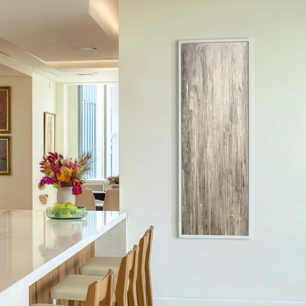 This vertical canvas wall art features an abstract design with a palette of gray and white, framed in white. It hangs on a plain wall in a room with a.