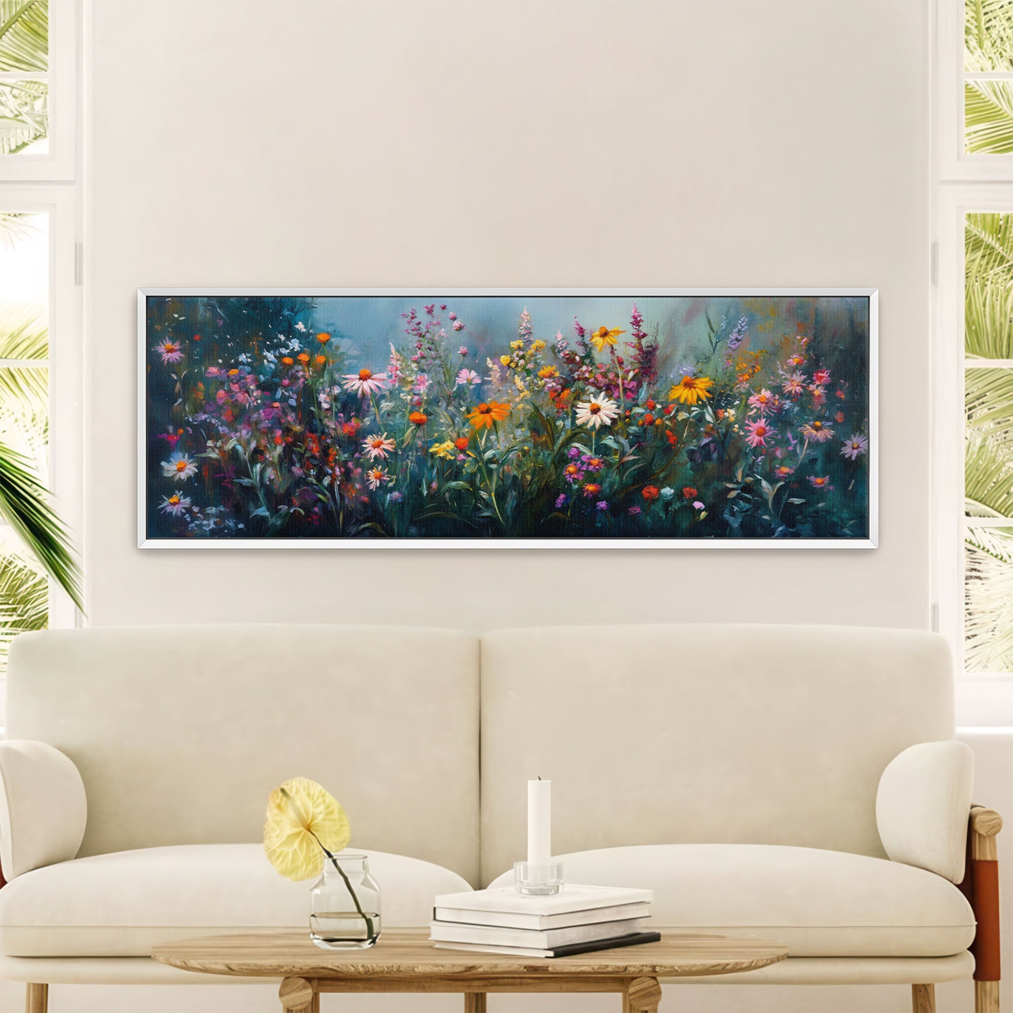 White-framed panoramic abstract floral painting featuring a vibrant field of wildflowers in various colors like orange, pink, purple, and white, against a deep blue-green background, hung above a cream sofa in a bright, modern living room
