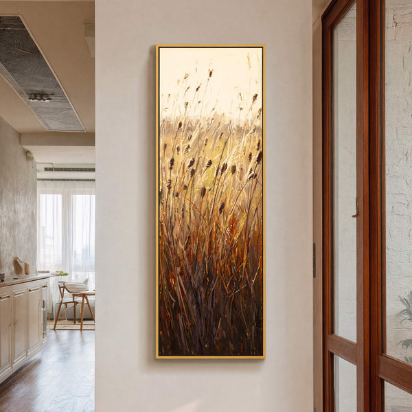 This vertical canvas wall art showcases a modern impressionist painting of reeds with a warm, golden palette, displayed on a light-colored wall next to a wooden door frame.