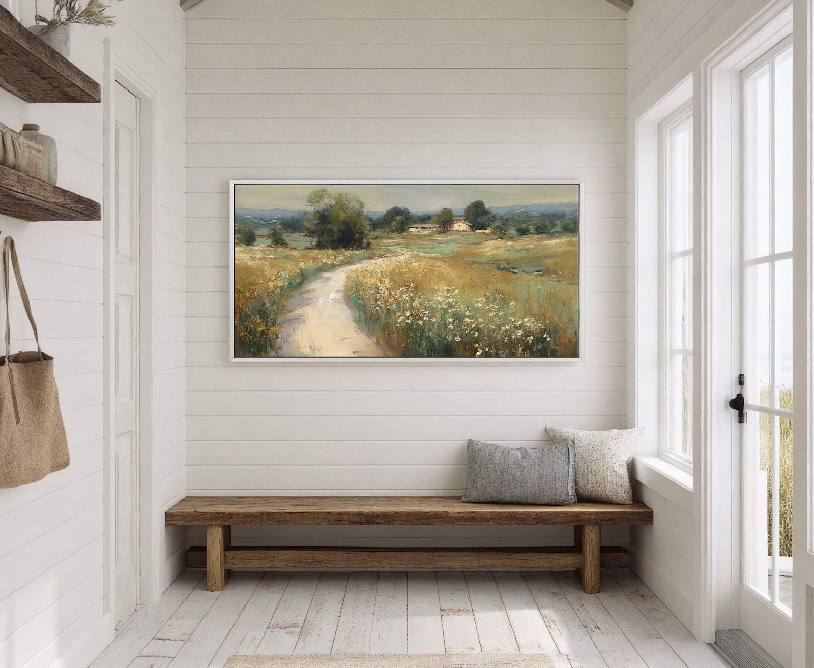 A horizontal, impressionistic landscape painting print of a country road winding through a field with scattered wildflowers, framed in white and displayed on a white paneled wall above a wooden.