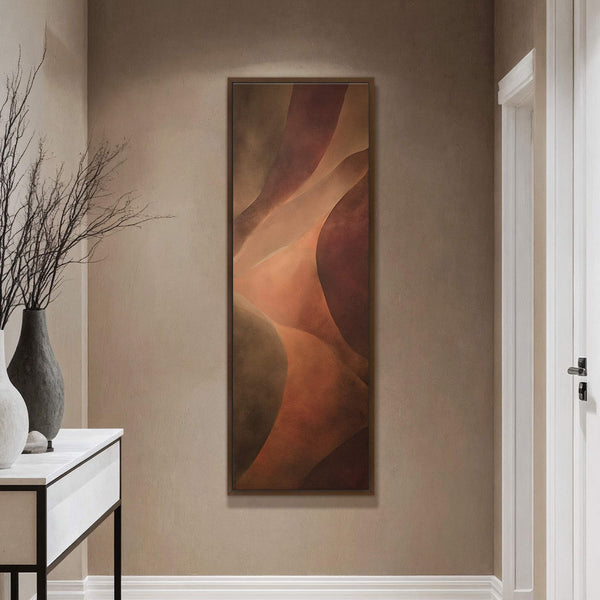 This vertical canvas wall art features abstract, wavy shapes in a warm palette of terracotta, brown, and orange, framed in dark wood and displayed on a tan wall next to.