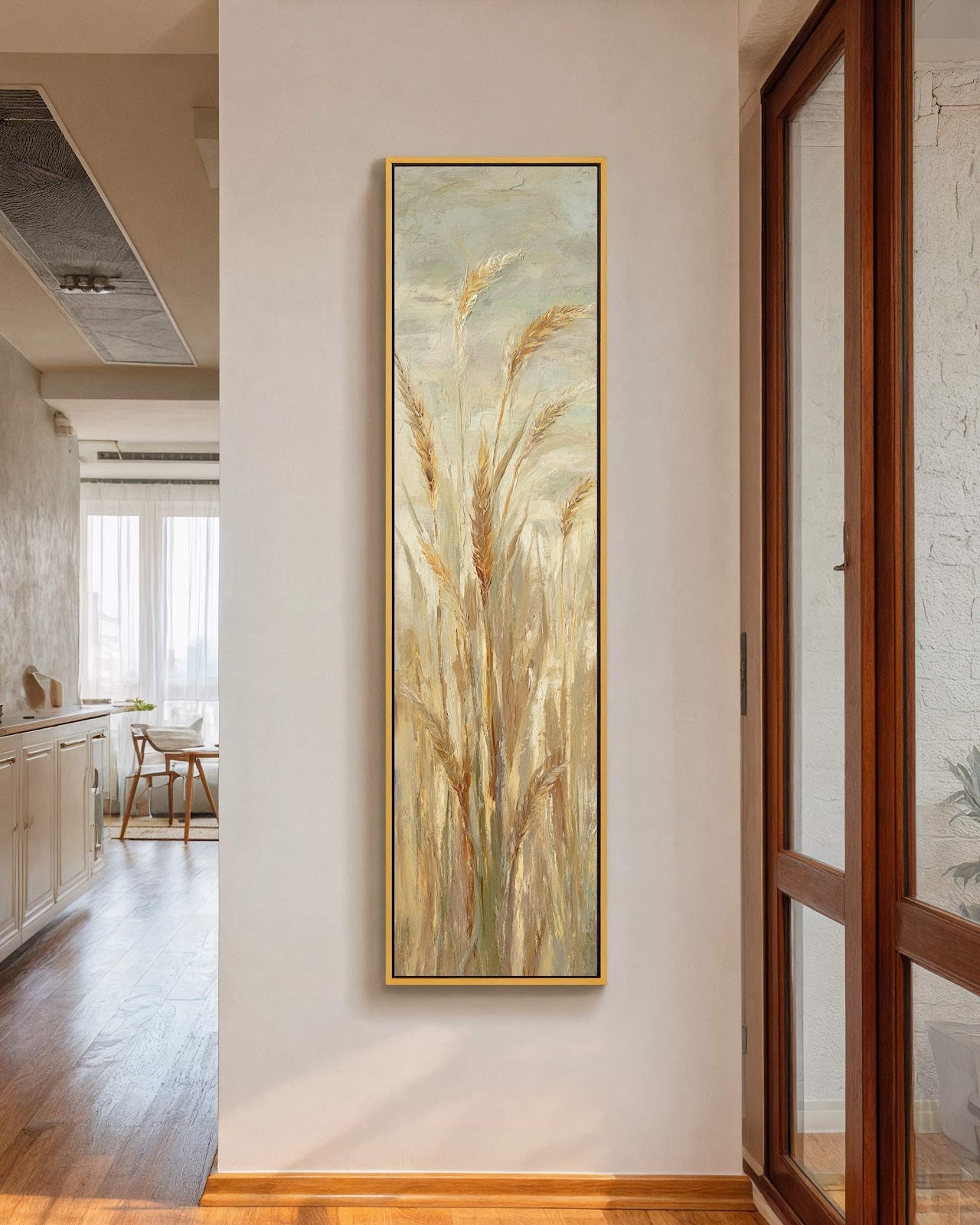 This vertical painting print showcases golden wheat stalks in an impressionistic style, hanging in a gold floater frame on a cream hallway wall near a wooden door frame.