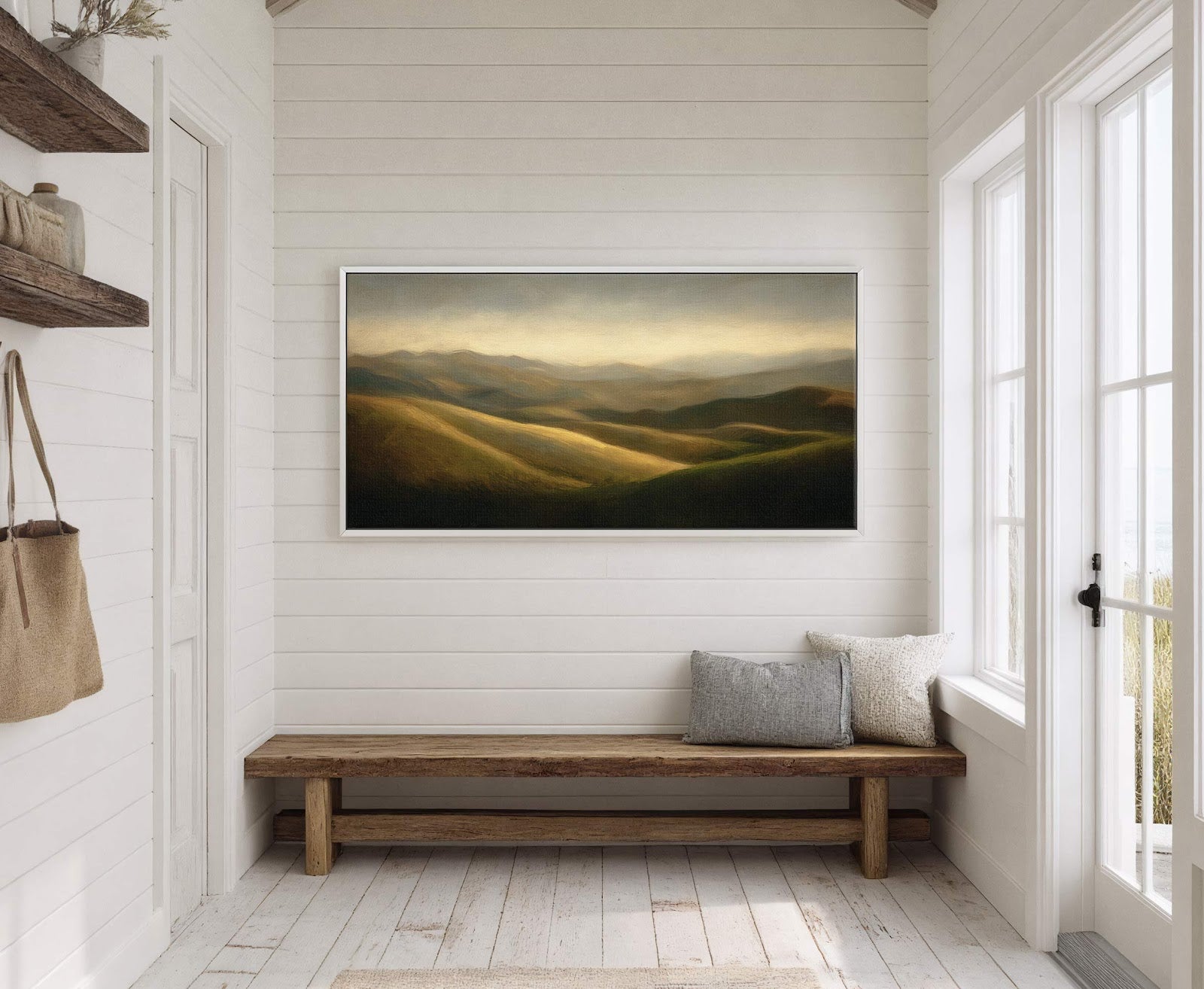 This horizontal canvas wall art features a landscape of rolling hills in a muted, earthy palette with dramatic lighting. It is displayed on a white paneled wall above a wooden.
