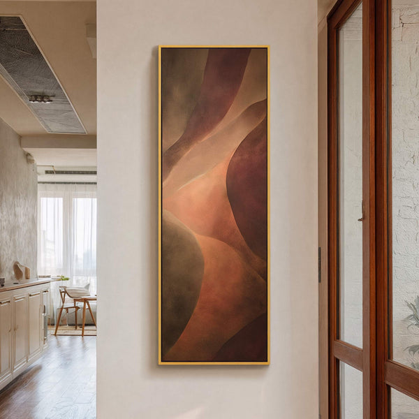 This vertical canvas wall art features abstract shapes in a warm, earthy palette of browns and oranges, framed in gold and displayed on a white wall, with a wooden door.