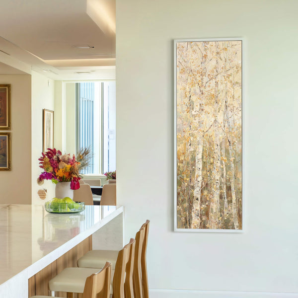 This vertical canvas print features an impressionistic painting of birch trees in a warm, golden palette, framed in white and hung on a pale wall next to a bar with.