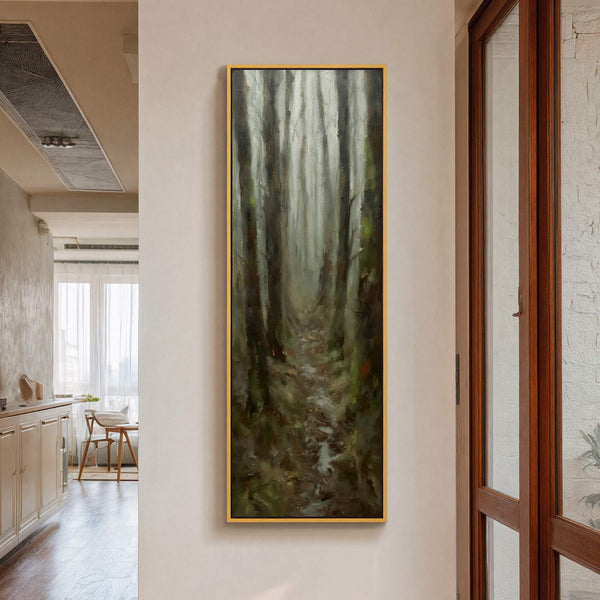 This vertical canvas print displays an impressionistic forest scene with a muted green and brown palette, framed in gold, hanging on a beige wall near a wooden doorway and interior.
