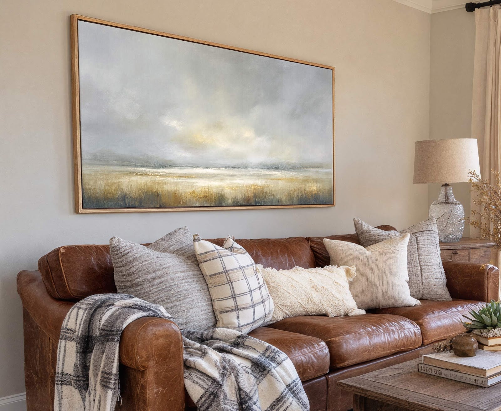 This horizontal, abstract landscape canvas wall art features a muted palette of grays, blues, and golds, depicting cloudy skies over a marshy field, framed in natural wood and hung above.