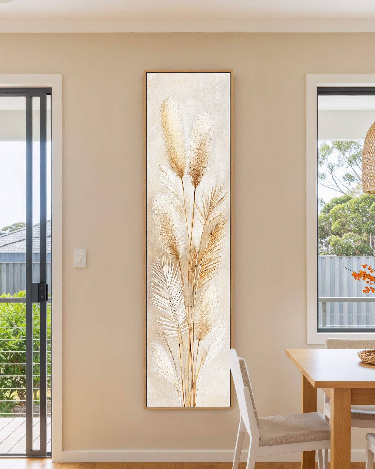 This vertical canvas art print showcases textured pampas grass in neutral tones, displayed in an oak floater frame on a beige dining room wall beside a wooden table.